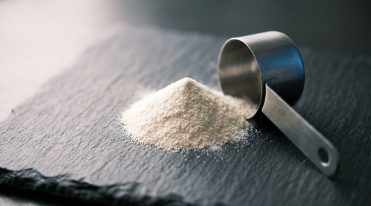 A small mound of fine white powder on dark slate beside a stainless steel scoop