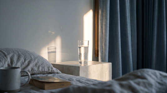 A glass of water on a bedside surface with morning light falling across it