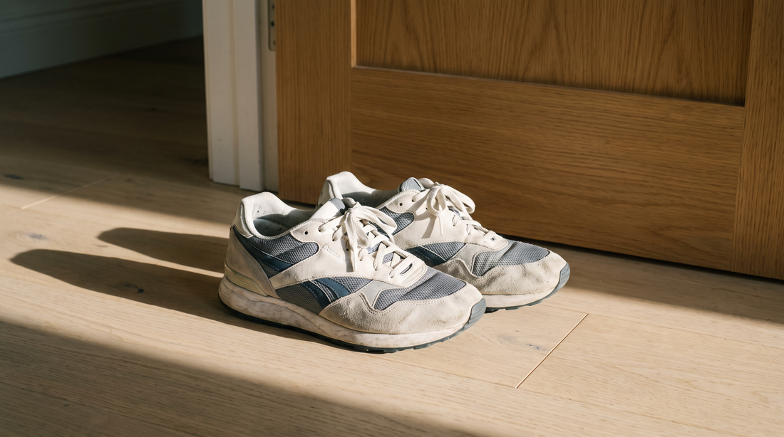 A worn pair of running shoes set down beside a door in early morning light